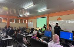 Sala de aula de telecentro com alunos dos cursos gratuitos de tecnologia da Prefeitura de Belo Horizonte, utilizando computadores, com monitores à frente. 