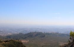 Imagem panorâmica de Belo Horizonte, aérea, com uma parte de vegetação e outra doe uma série de edificações, ao fundo. Dia claro, com uma percepção de névoa de poeira.