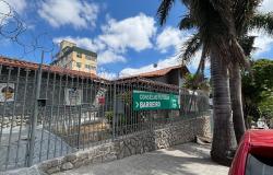 Fotografia externa, durante o dia, da fachada de um imóvel onde funciona o Conselho Tutelar Barreiro. O prédio é cercado por um muro baixo de pedras e um portão de grades metálicas, sobre o qual há várias voltas de arame farpado. Ao centro da imagem, preso às grades, há uma grande placa verde com a inscrição “CONSELHO TUTELAR BARREIRO”, acompanhada de uma seta apontando para a direita e da identidade visual da Prefeitura de Belo Horizonte.