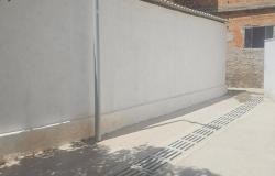 imagem mostra o trecho de uma rua com um muro branco do lado esquerdo e uma grade no piso.