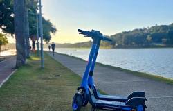 Patinete elétrico na cor azul, ao fundo, Lagoa da Pampulha e pôr-do-sol, enquanto pessoas correm e caminham na Orla da Lagoa da Pampulha