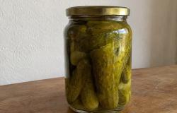 Imagem mostra um vidro com conserva de pepino disposto em cima de uma mesa de madeira.