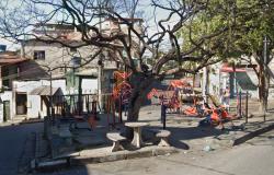 Imagem mostra uma praça circular com brinquedos, mesa, bancos e uma árvore. Hácasas em volta.