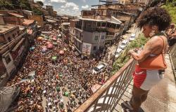 Bloco Seu Vizinho desfila pelas ruas de Belo Horizonte, acompanhado por grande público, enquanto uma das integrantes acompanha a apresentação.