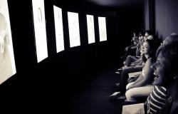 A imagem em preto e branco, mostram a reação de um público durante uma exposição ou instalação audiovisual. 