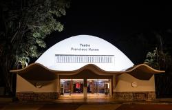 Fotografia noturna da fachada do Teatro Francisco Nunes. A edificação branca e iluminada se destaca contra o fundo escuro do céu e das árvores ao redor. O prédio possui uma grande cobertura abobadada e, na entrada frontal, uma marquise com ondulações modernas sobre as portas de vidro iluminadas. No topo da fachada branca, lê-se o nome "Teatro Francisco Nunes" em letras escuras.