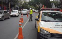 Imagem mostra um funcionário da BHTrans controlando o trãnsito. De um lado há uma viatura e do outro carros em movimento.