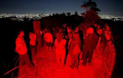 Imagem mostra um grupo de pessoas no escuro observando a cidade iluminada ao fundo.