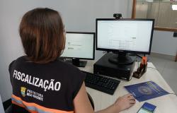 Mulher que atua na Fiscalização da PBH, usando colete, trabalha no computador