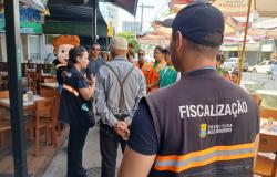 Servidores da Fiscalização, usando coletes de trabalho, conversam com comerciantes na Rua Alberto Cintra em frente a um estabelecimento comercial.