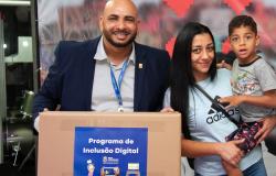 Mulher com criança no colo recebe caixa contendo computador de representante da Prodabel 