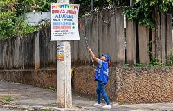 Agente da Fiscalização, usando colete e boné azul, retira cartaz de poste. 