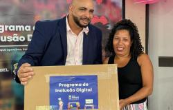Um homem e uma mulher ladeados, em que ele entrega uma caixa contendo computador à ela, ambos com semblantes sorridentes