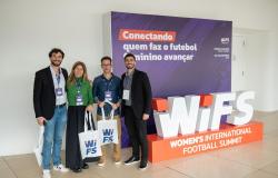 Três homens e uma mulher, todos representantes da Belotur, estão ao ldo de um estande da Women’s International Football Summit (Wifs). Todos carregam sacolas alusivas ao evento. A mulher está de blusa verde, dois homens estão de blaser escuro e o outro de camisa azul.