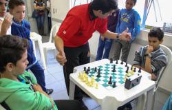 Crianças jogam xadrez acompanhada por um adulto.