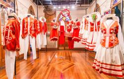 Dez trajes folclóricos, masculinos e femininos, nas cores branco e laranja, expostos em sala do Museu de Moda.
