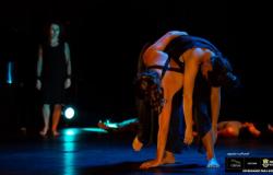 Dois bailarinos dançam com os corpos de um sobre o outro, e um terceiro observa. 