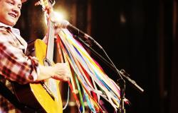 Homem toca violão com fitas coloridas amarradas