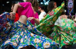 Duas mulheres dançam e agitam saias coloridas de chita, durante o dia. 