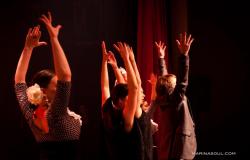 Duas mulheres e dois homens erguem as mãos, em um gesto tipico da dança flamenca, sob luz avermelhada. 