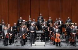 Imagem de todos os componentes da Orquestra Sinfônica no palco de um teatro