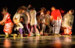 Imagem de pessoas dançando em um palco. Foto feita em modo que demonstra movimento