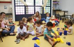 Oito crinças brincam em sala de UMEI, acompanhadas de duaseducadoras infantis.