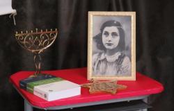 Foto de Anne Frank ao lado de livro, estrela de david e chanuquiá, o candelabro judaico, sobre uma mesa de forro vermelho. Foto ilustrativa. 