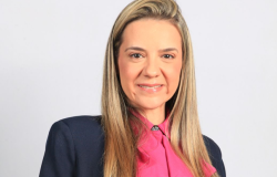 Mulher loira usando blusa rosa e casaco azul, sorri para a foto