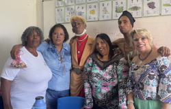 #paratodosverem: Um grupo de seis pessoas, a maioria professoras e funcionárias, posa abraçado em uma sala de aula. A cena, em frente a um quadro com o alfabeto, sugere um momento de confraternização e celebração pedagógica, com um toque criativo e festivo.