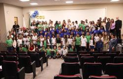 #paratodosverem: Grande grupo de estudantes e educadores se reunem em um auditório para uma foto posada. Crianças e jovens, muitos usando camisetas verdes, azuis e brancas, posam sorridentes ao lado de professores e convidados.