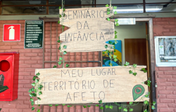 #paratodosverem: Porta de entrada da escola decorada com placas de madeira escritas “Seminário da infância” e “Meu lugar território de afeto”