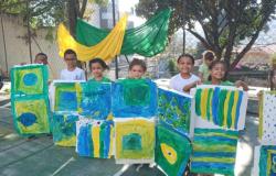#paratodosverem: Crianças exibem pinturas em tons de verde, amarelo e azul durante atividade ao ar livre. Os trabalhos são inspirados nas cores da bandeira do Brasil e estão organizados lado a lado. Ao fundo, tecidos verde e amarelo decoram o espaço.