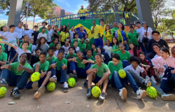 #paratodosverem: Grupo de estudantes, professores e monitores do PEI posam para foto em uma praça. A maioria veste camisetas verdes, brancas e amarelas e alguns seguram bolas, bambolês. Uma bandeira do Brasil aparece ao fundo. 