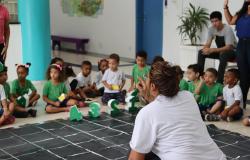  imagem mostra um grupo de crianças vestindo camisetas verdes e brancas, participando de uma atividade educacional em um ambiente escolar.