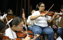 Estudantes de uniforme tocam violinos em uma sala com fundo preto