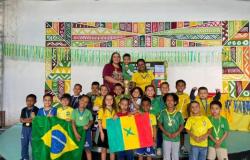 #paratodosverem: Várias crianças posam para uma foto vestidas com as cores verde e amarelo e com medalhas no pescoço. Na frente, duas crianças seguram as bandeiras do Brasil e de Senegal. Ao fundo, duas professoras acompanham o grupo, com um troféu erguido por um dos estudantes.