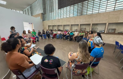 Várias pessoas participam de uma roda de conversa, sentadas em cadeiras dispostas em círculo, em uma sala.