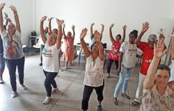 Mais de dez idosos fazem ginástica de pé com as mãos para cima; foto ilustrativa do Programa Vida Ativa.