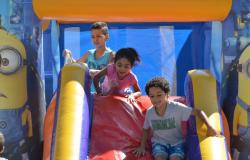 Três crianças descem em escorregador inflável durante o dia. 