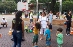 Três crianças jogam basquete, acompanhadas por dois adultos.