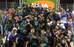 Mais de trinta pessoas, entre membros de um time de futebol e torcedores, comemoram a vitória de uma categoria da Copa Centenário. 