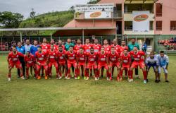 Time de futebol com uniforme vermelho e mais de 20 integrantes posa para foto. 