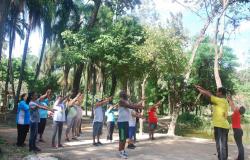 Cerca de dez pessoas fazem ginástica em contato com a natureza, orientadas por dois técnicos da Prefeitura. 
