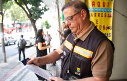 Fiscal de colete da Prefeitura de Belo Horizonte analisa um documento impresso na calçada durante ação de fiscalização de poluição visual na cidade.
