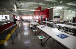 Vista interna do Restaurante Popular, em BH, com mesas e bancos organizados no salão de refeições, área de distribuição de alimentos, piso tátil para acessibilidade e funcionários realizando atividades no local.