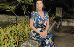 Foto oficial - Laura Maria Moraes Mourão, Diretora de Gestão e Educação Ambiental Diretora de Gestão e Educação Ambiental - Laura Maria Moraes Mourão, posa em uma fotografia ao lado de plantas e um vestido azul estampado de plantas.