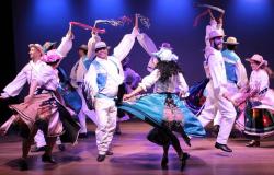 Grupo folclórico Aruanda em apresentação: cerca de cinco casais com roupas folclóricas dançam, em apresentação teatral. 