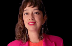 Diretora de Promoção das Artes da Fundação Municipal de Cultura - Paula Senna, posa em uma fotografia com camisa tom de laranja e um palito tom rosa escuro.