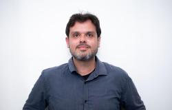 Homem branco, cabelo preto, barba grisalha, camisa azul escuro.